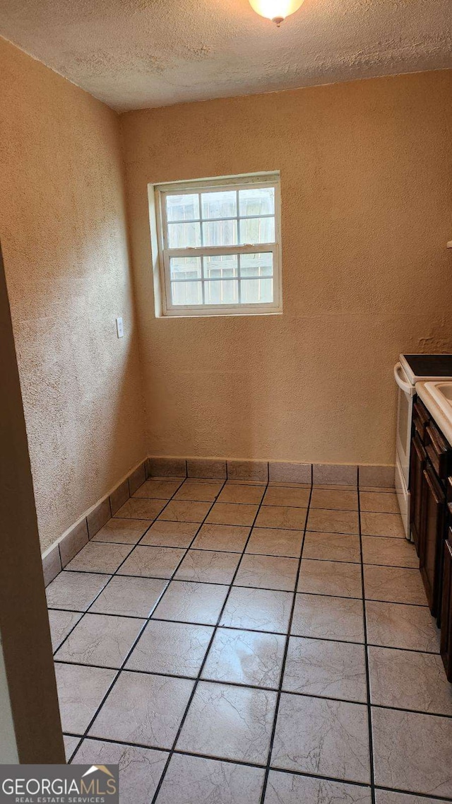 empty room with light tile patterned floors, a textured ceiling, and a textured wall