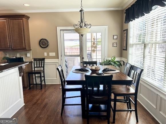 dining room with a decorative wall, wainscoting, crown molding, and dark wood-style flooring