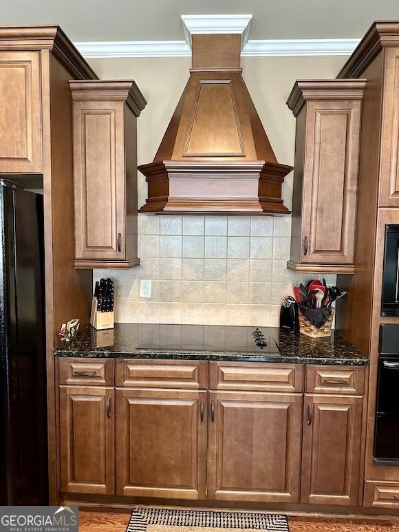 kitchen with backsplash, crown molding, dark stone counters, custom exhaust hood, and black appliances