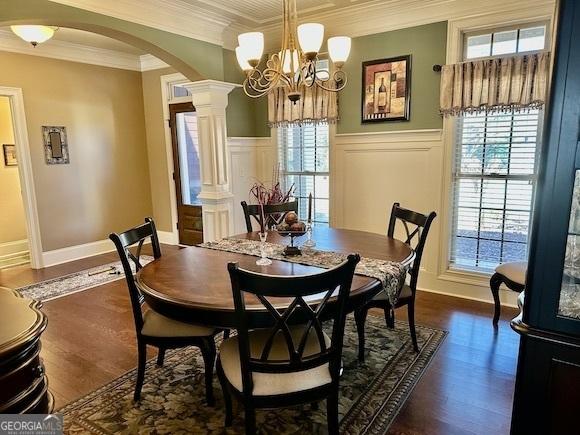 dining space with decorative columns, arched walkways, dark wood-style flooring, and crown molding