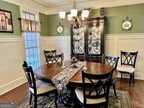 dining area with a wainscoted wall, dark wood-type flooring, ornamental molding, a decorative wall, and a chandelier