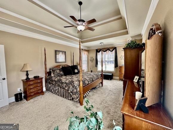 carpeted bedroom with baseboards, a raised ceiling, a ceiling fan, and crown molding