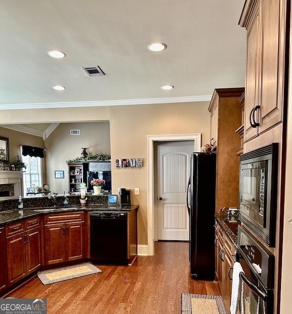 kitchen featuring visible vents, dark wood-type flooring, ornamental molding, black appliances, and a sink