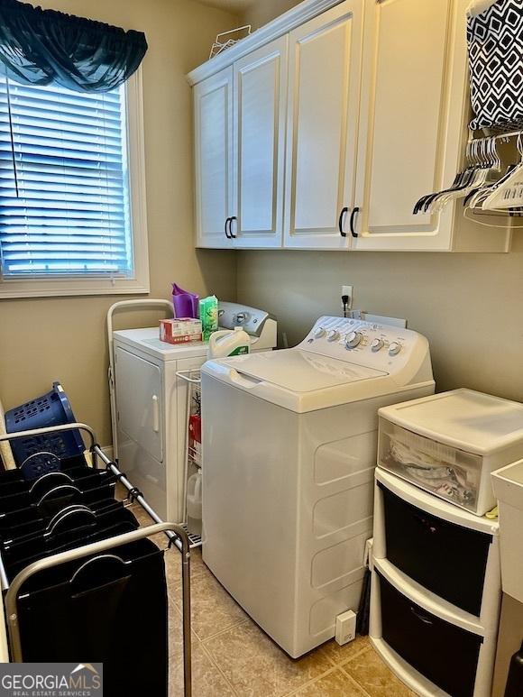 clothes washing area featuring washer and clothes dryer, light tile patterned floors, and cabinet space