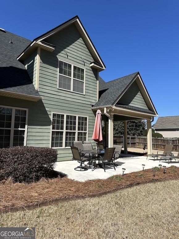 back of property with a patio area, fence, and a shingled roof