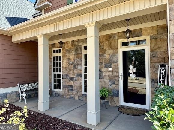 view of exterior entry featuring stone siding and a shingled roof