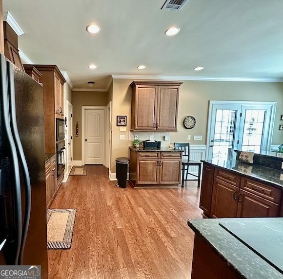 kitchen featuring dark stone countertops, visible vents, light wood finished floors, black appliances, and crown molding