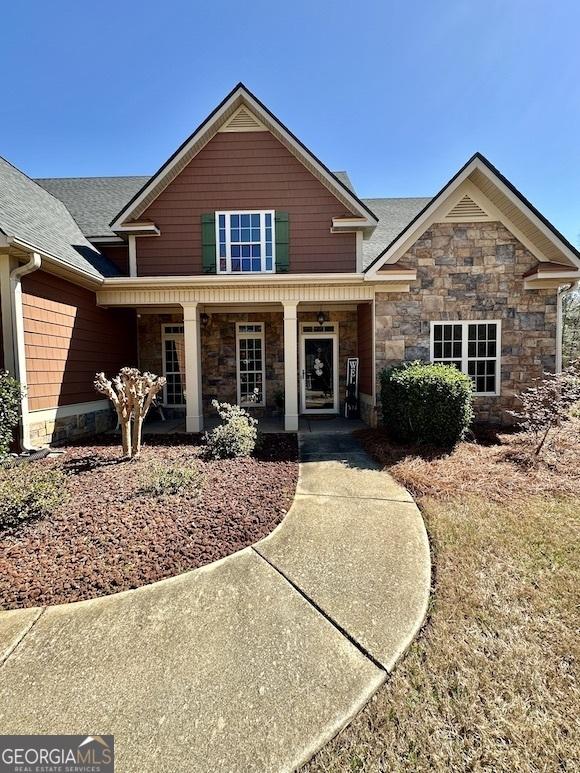 craftsman inspired home featuring stone siding, roof with shingles, and a porch