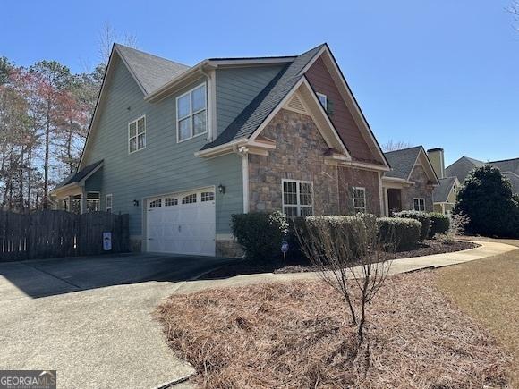 view of side of home featuring an attached garage, fence, stone siding, and driveway