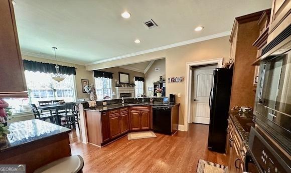 kitchen with visible vents, brown cabinets, a peninsula, wood finished floors, and black appliances