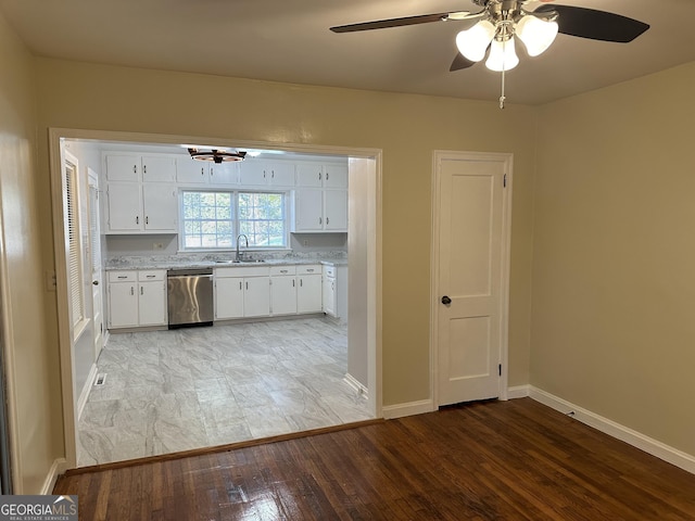 kitchen with a sink, stainless steel dishwasher, white cabinets, light wood finished floors, and baseboards