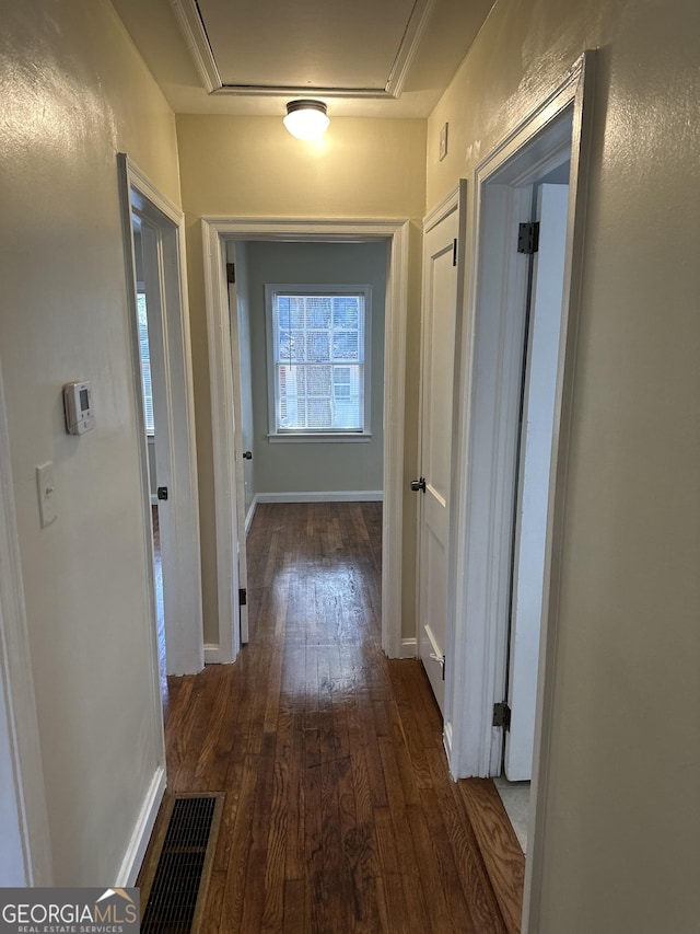 hallway with dark wood finished floors, visible vents, and baseboards