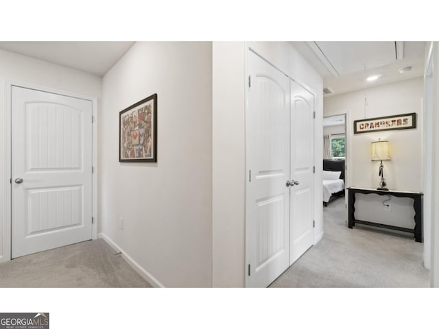 hallway with visible vents, light colored carpet, attic access, and baseboards