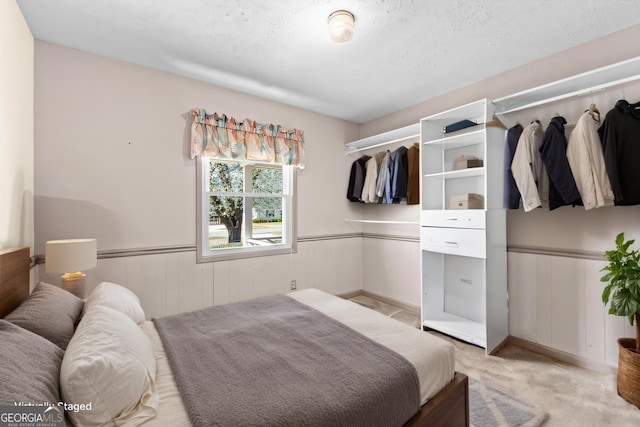 bedroom with a wainscoted wall, light carpet, and a textured ceiling