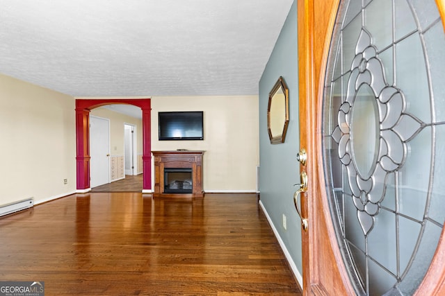 unfurnished living room featuring a textured ceiling, wood finished floors, arched walkways, a fireplace, and decorative columns