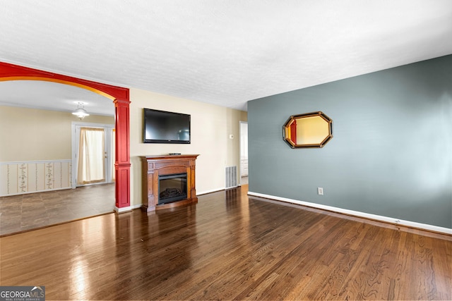 unfurnished living room featuring a glass covered fireplace, decorative columns, wood finished floors, and visible vents