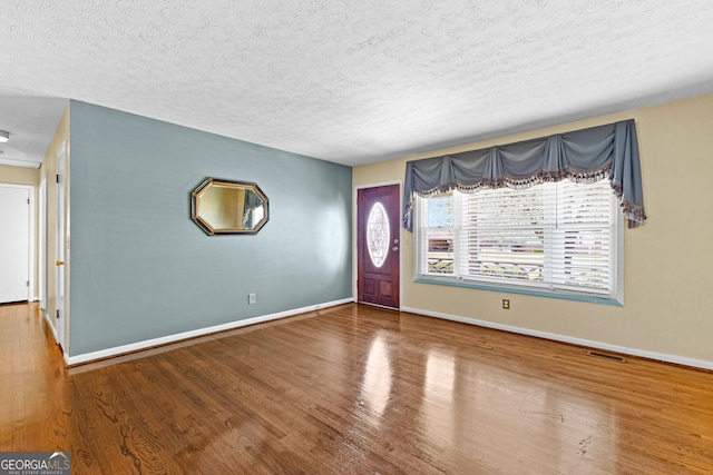 foyer entrance featuring visible vents, baseboards, a textured ceiling, and wood finished floors