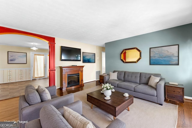 living room with visible vents, a glass covered fireplace, wood finished floors, baseboards, and ornate columns