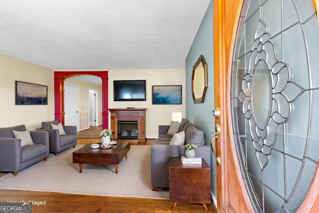 living area with arched walkways, a fireplace, ornate columns, and wood finished floors