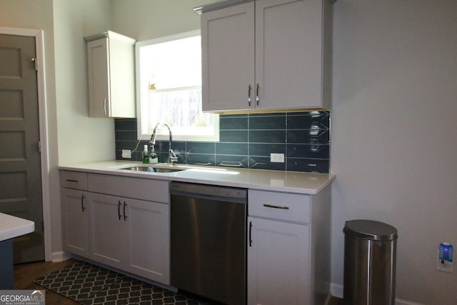 kitchen with stainless steel dishwasher, decorative backsplash, light countertops, and a sink