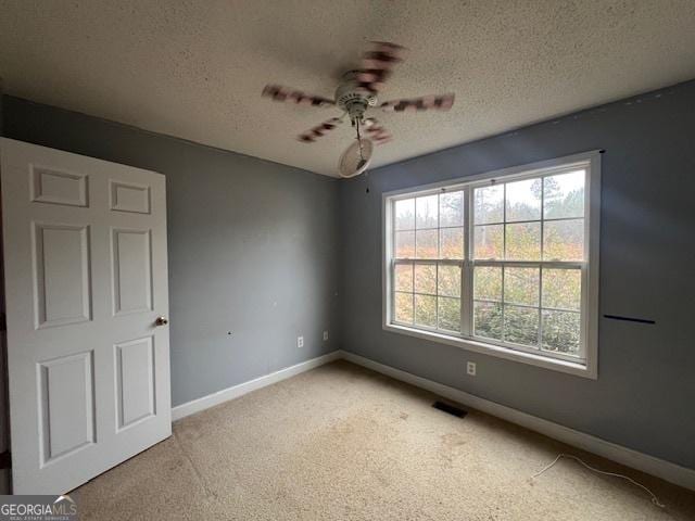 spare room with visible vents, baseboards, ceiling fan, light colored carpet, and a textured ceiling