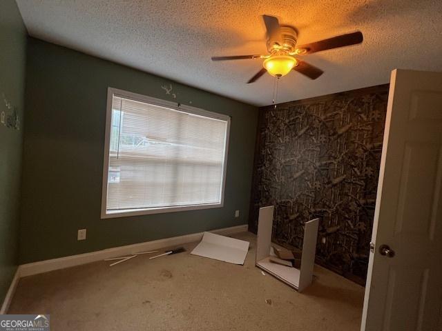 spare room with baseboards, ceiling fan, a textured ceiling, and carpet