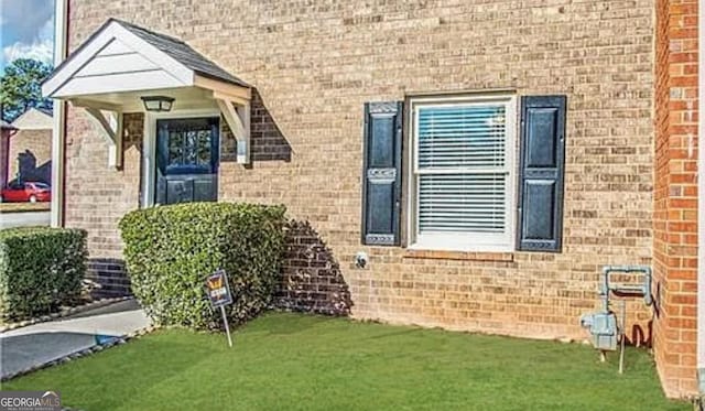 doorway to property featuring a lawn and brick siding