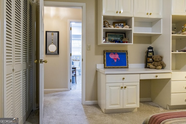 interior space featuring baseboards, light colored carpet, and built in desk