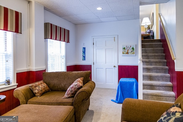 carpeted living room featuring a drop ceiling, wainscoting, and stairs