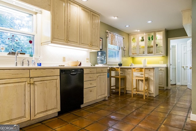 kitchen featuring glass insert cabinets, black dishwasher, light brown cabinets, and a sink