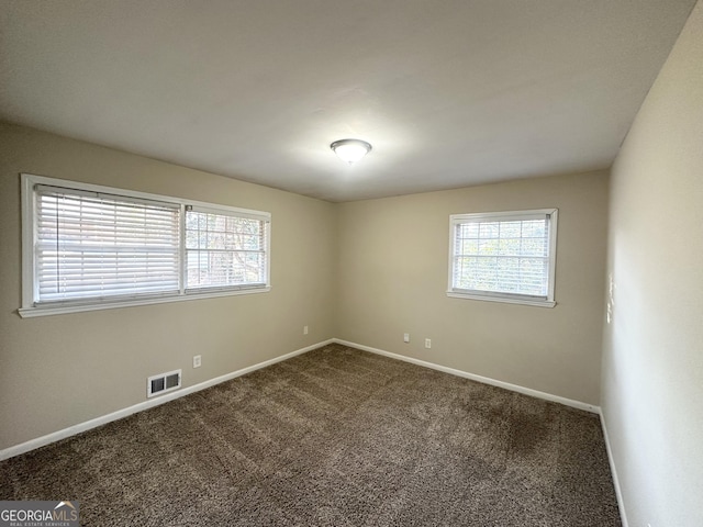 spare room featuring a healthy amount of sunlight, visible vents, dark colored carpet, and baseboards