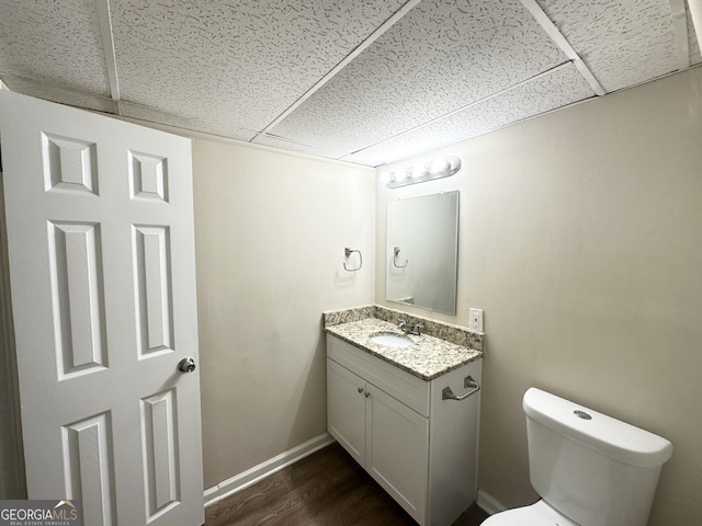 bathroom with baseboards, toilet, wood finished floors, vanity, and a paneled ceiling