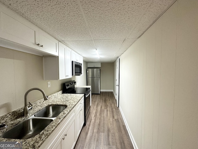 kitchen with a sink, wood finished floors, appliances with stainless steel finishes, white cabinets, and a paneled ceiling