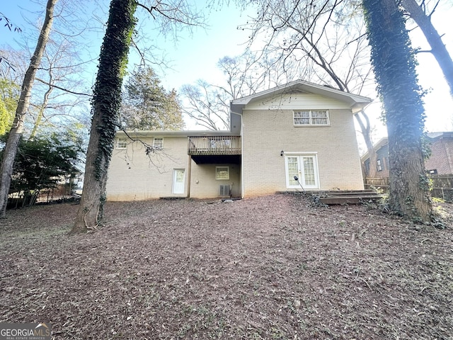 rear view of property featuring brick siding, french doors, a wooden deck, and fence