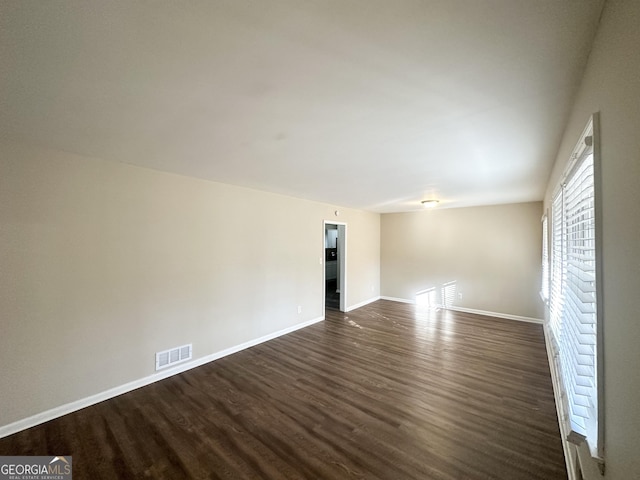 unfurnished room featuring visible vents, dark wood-type flooring, and baseboards