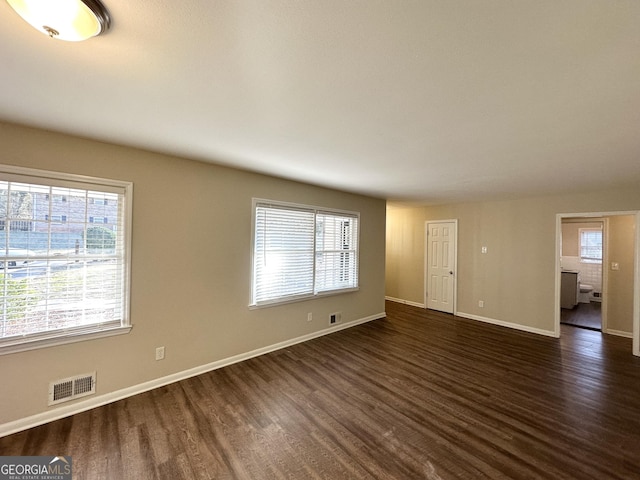 empty room featuring visible vents, a healthy amount of sunlight, dark wood-type flooring, and baseboards