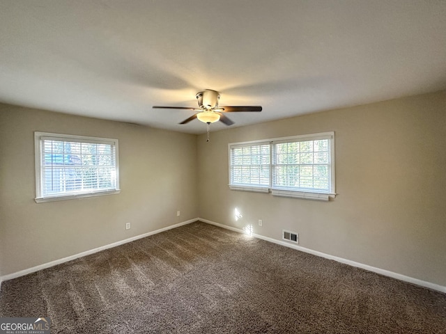 spare room featuring dark colored carpet, visible vents, baseboards, and a healthy amount of sunlight