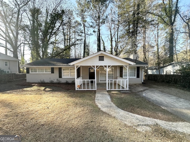 view of front facade featuring brick siding, covered porch, a chimney, and a front yard