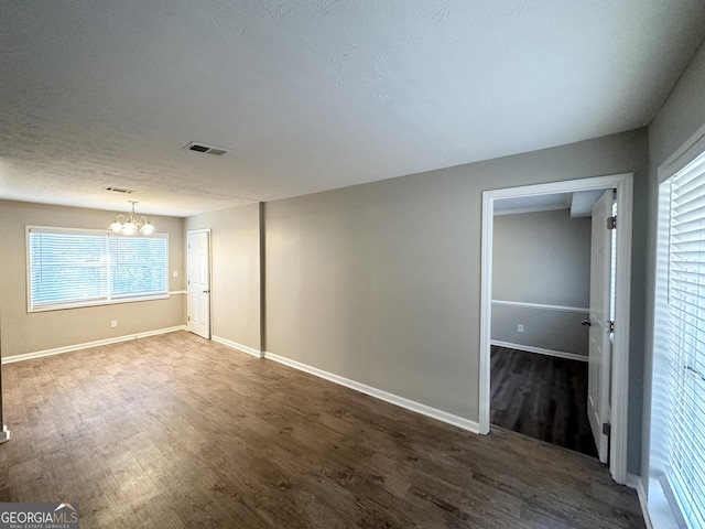 unfurnished room featuring dark wood-style floors, visible vents, baseboards, and a notable chandelier