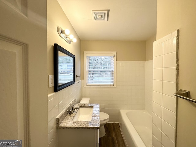 bathroom featuring visible vents, toilet, vanity, a bath, and tile walls