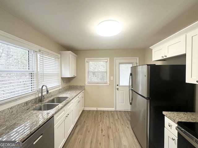 kitchen featuring light stone counters, light wood finished floors, a sink, white cabinets, and appliances with stainless steel finishes