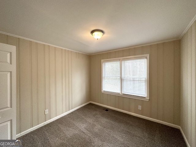 spare room featuring visible vents, baseboards, ornamental molding, and dark carpet