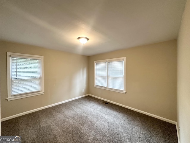 spare room featuring visible vents, baseboards, and dark colored carpet