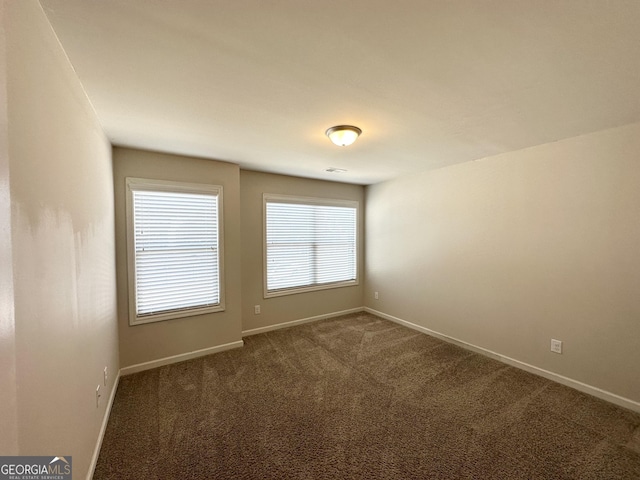empty room featuring dark colored carpet and baseboards
