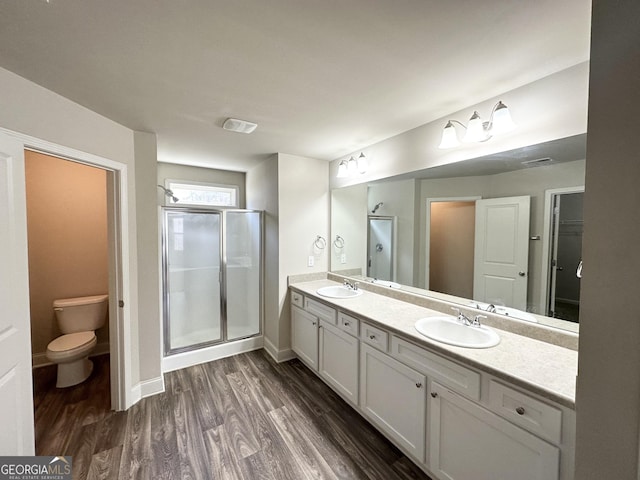 bathroom with toilet, a stall shower, a sink, wood finished floors, and double vanity