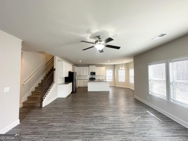 unfurnished living room with a ceiling fan, baseboards, visible vents, dark wood-style flooring, and stairs