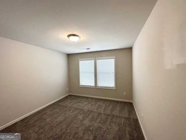 spare room with visible vents, baseboards, and dark carpet