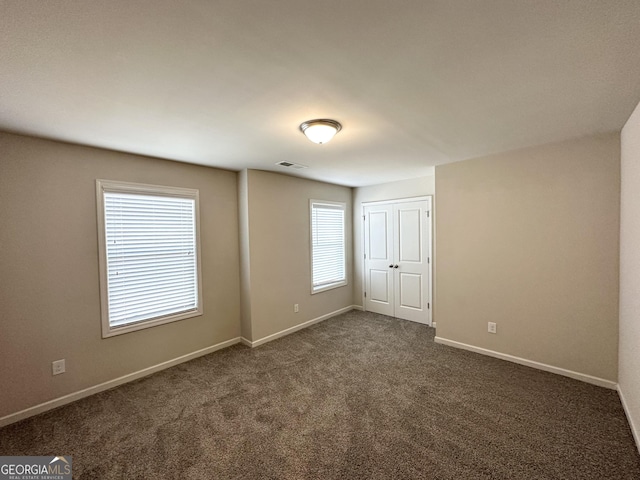 unfurnished room with visible vents, baseboards, and dark colored carpet