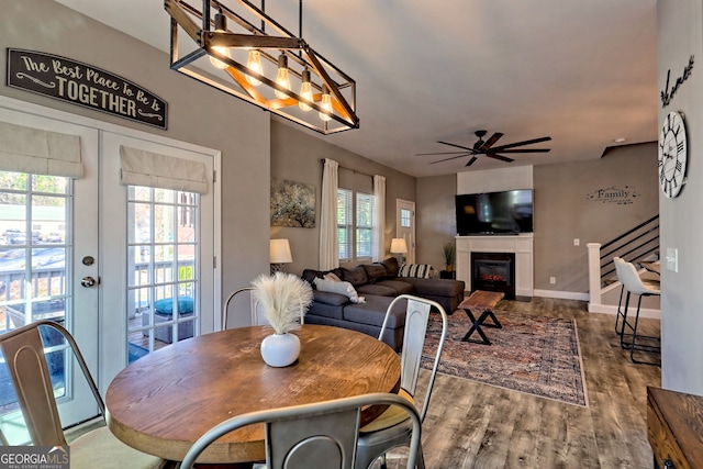 dining area with stairway, ceiling fan with notable chandelier, french doors, wood finished floors, and a glass covered fireplace