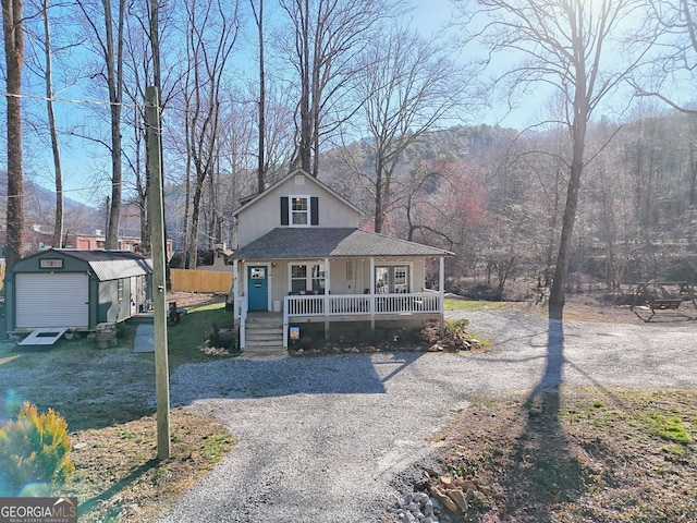 view of front of property featuring a shed, roof with shingles, gravel driveway, covered porch, and an outdoor structure